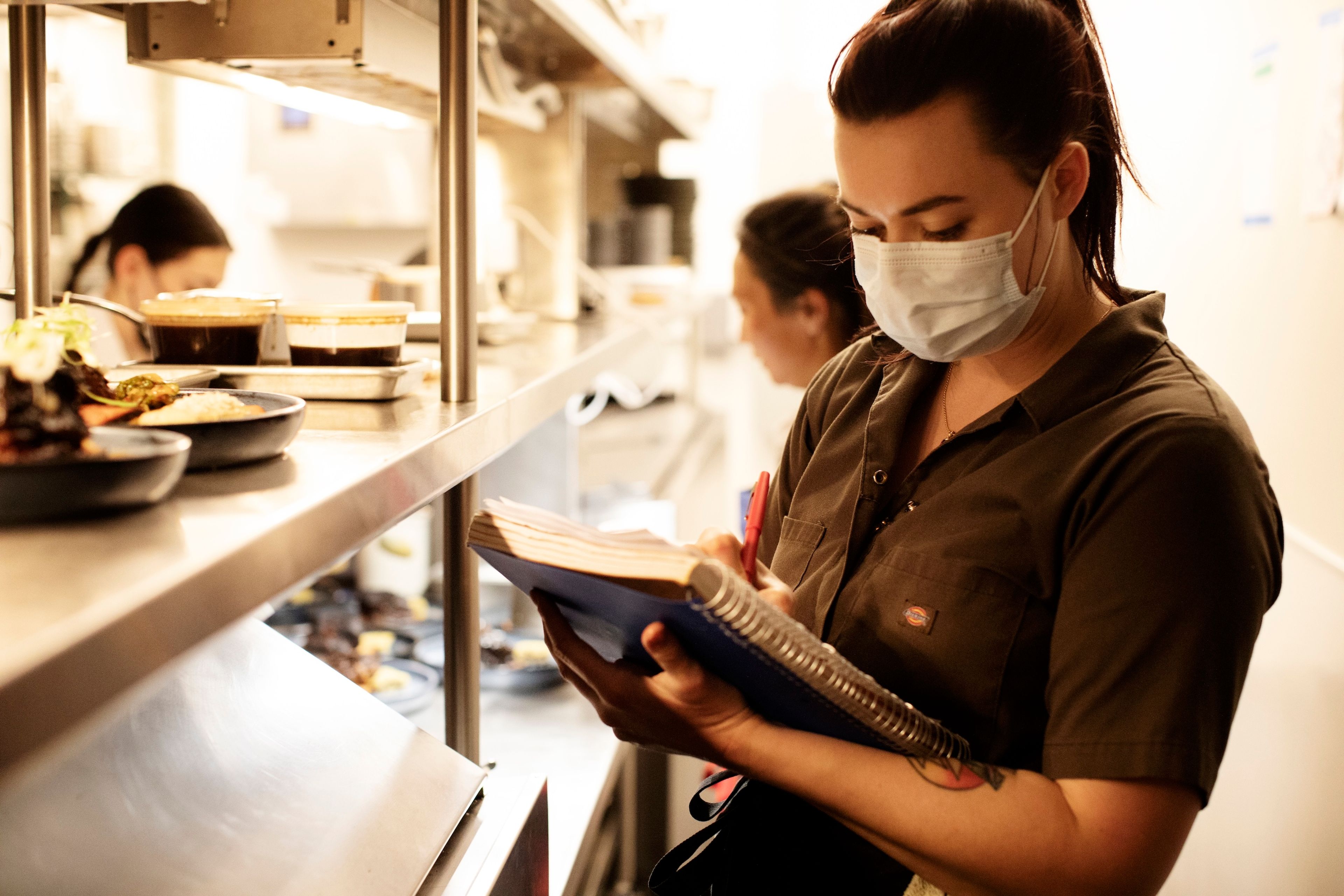 Woman next to a kitchen pass writes in a notebook