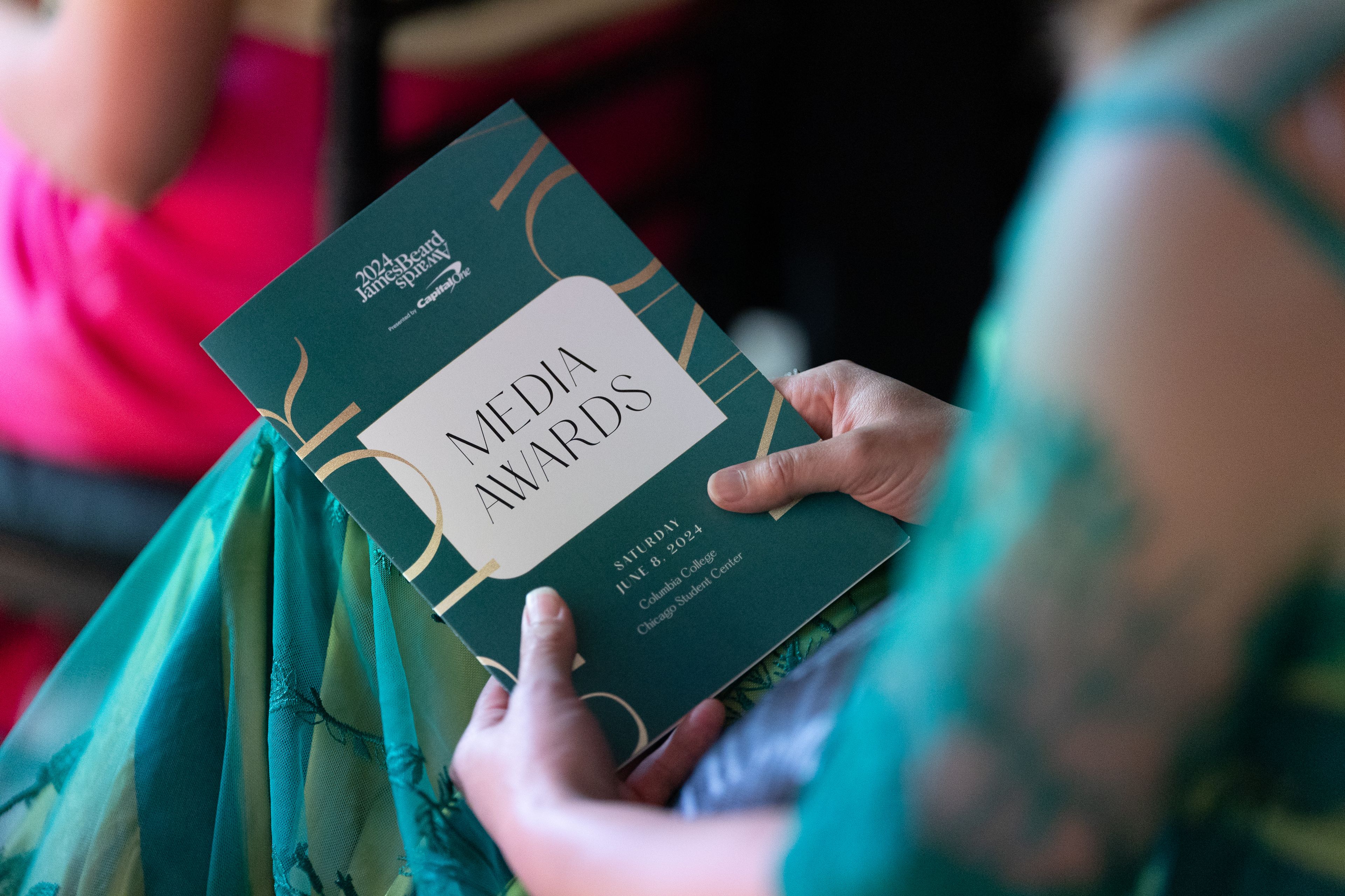 A woman seated, holding a booklet that says Media Awards