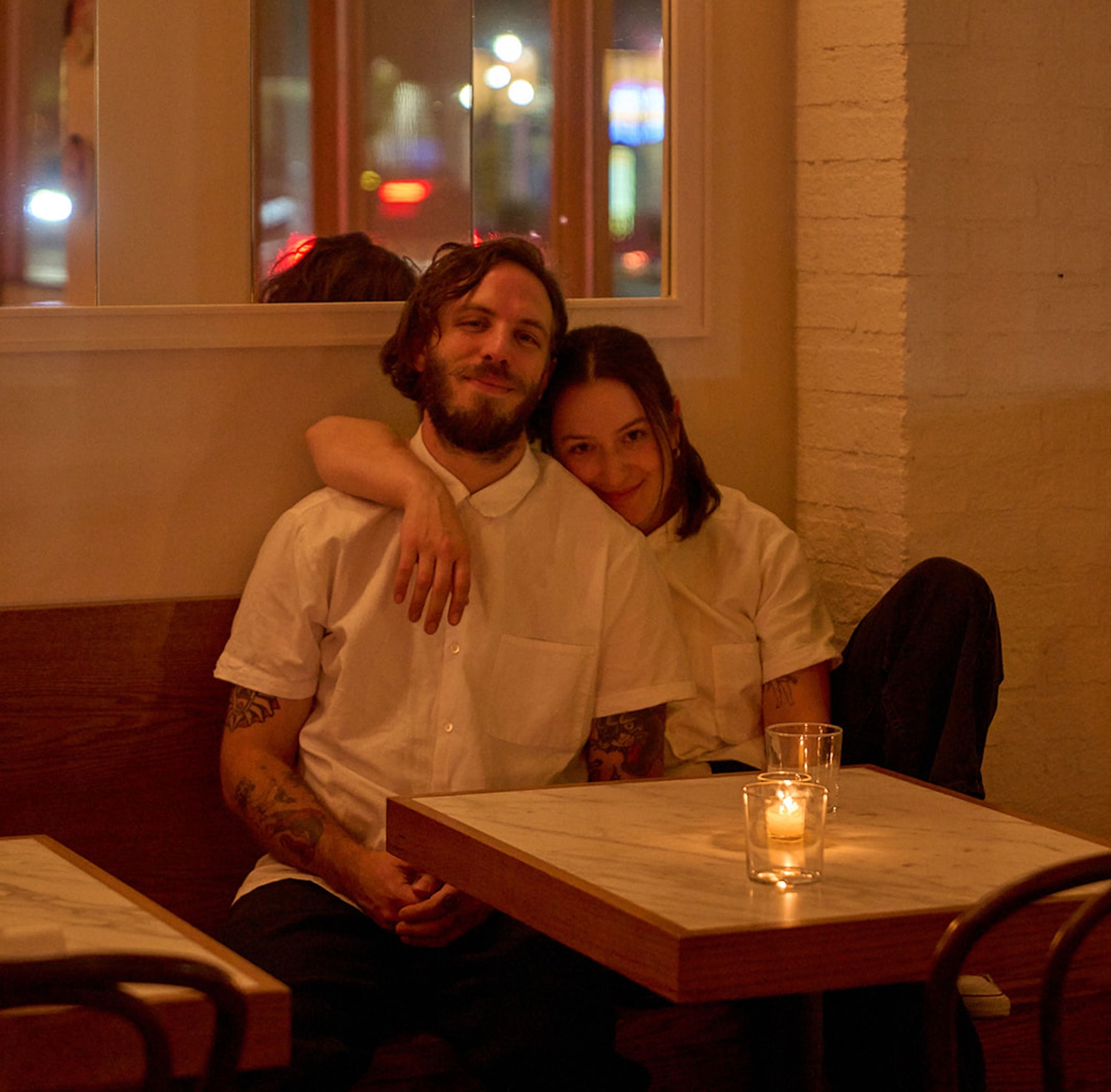 Anna Sonenshein and Niki Vahle seated at a restaurant table. Anna drapes her arm over Niki's shoulder.
