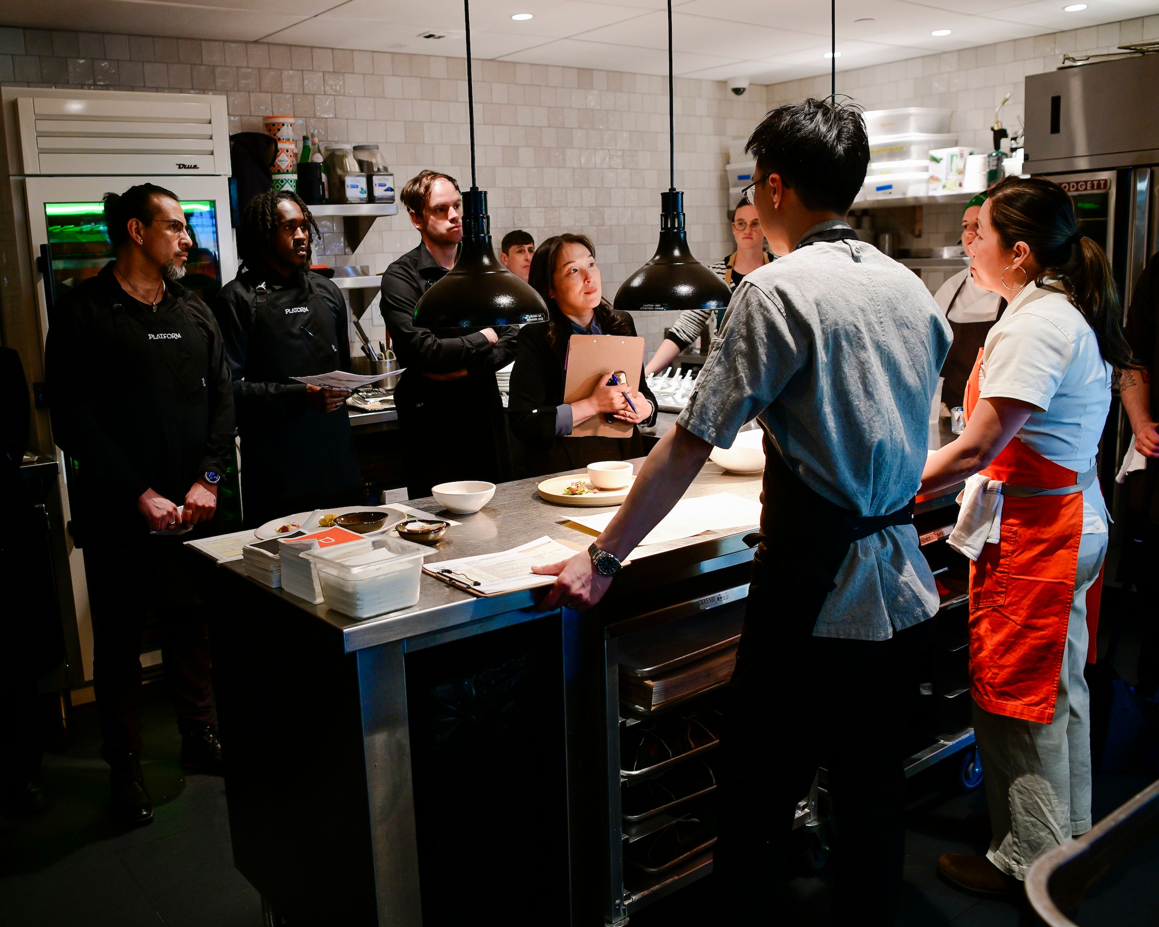 A group of chefs and servers stand in a kitchen