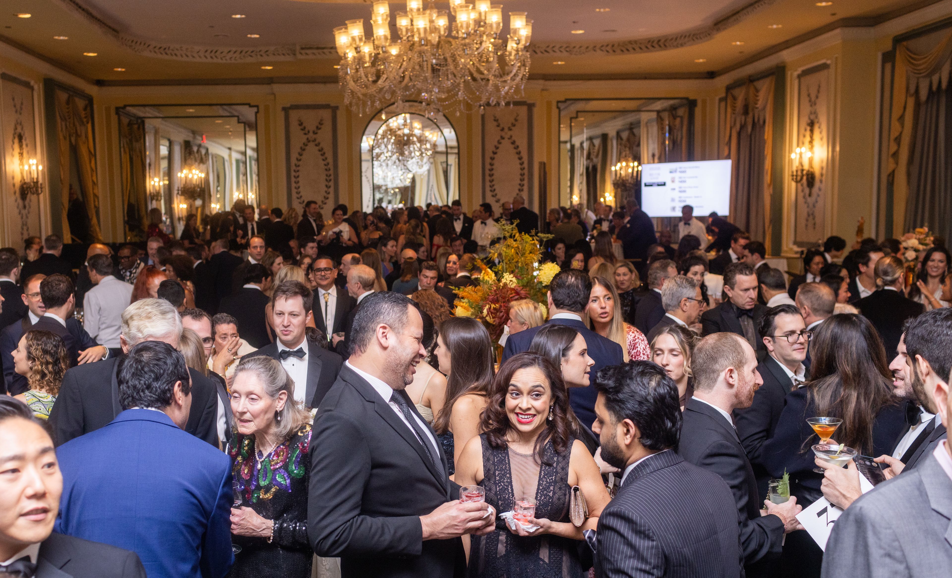 Crowd of people in black tie mingling in a luxury hotel ballroom