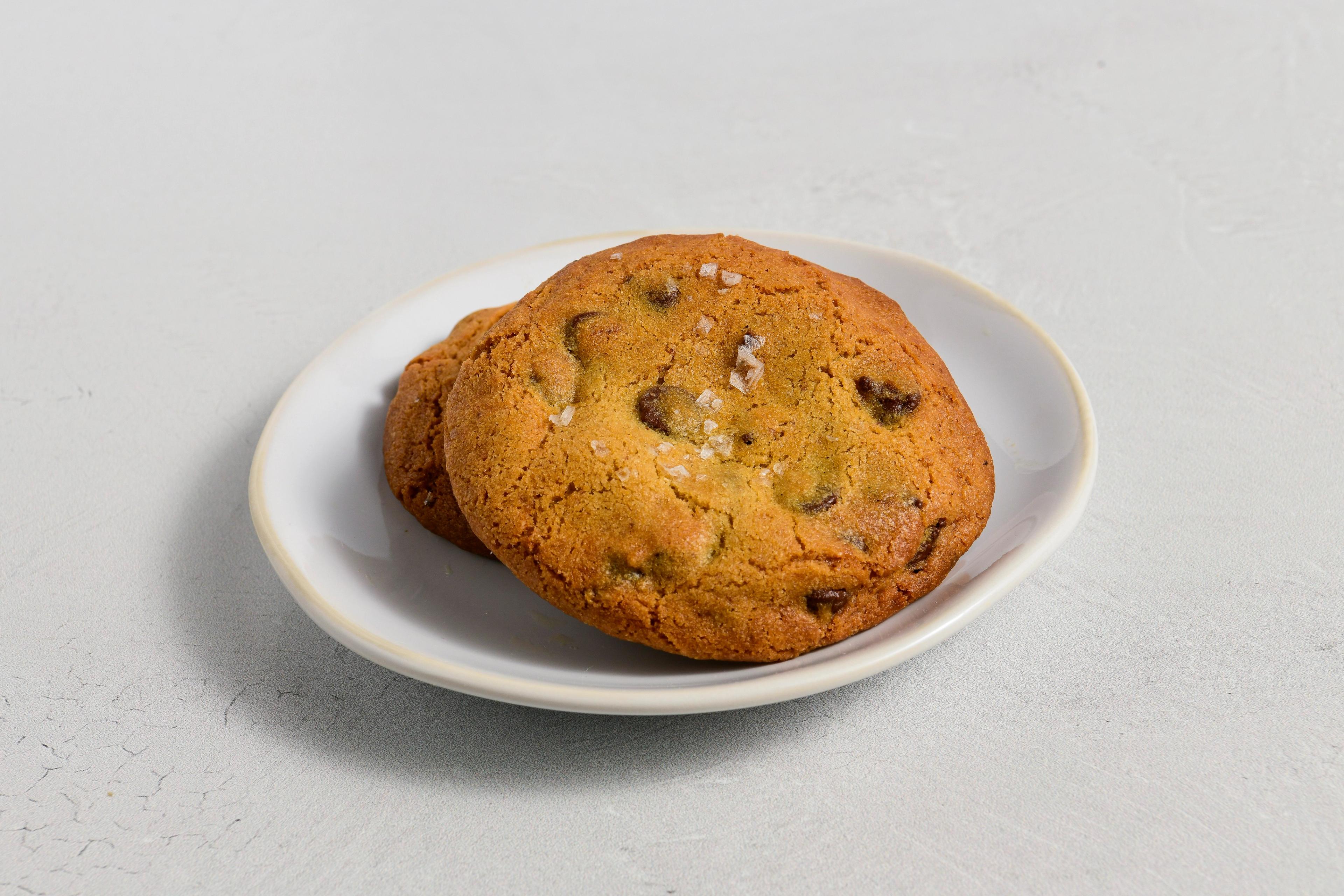 Two chocolate chip cookies with flaky salt on top on a white plate