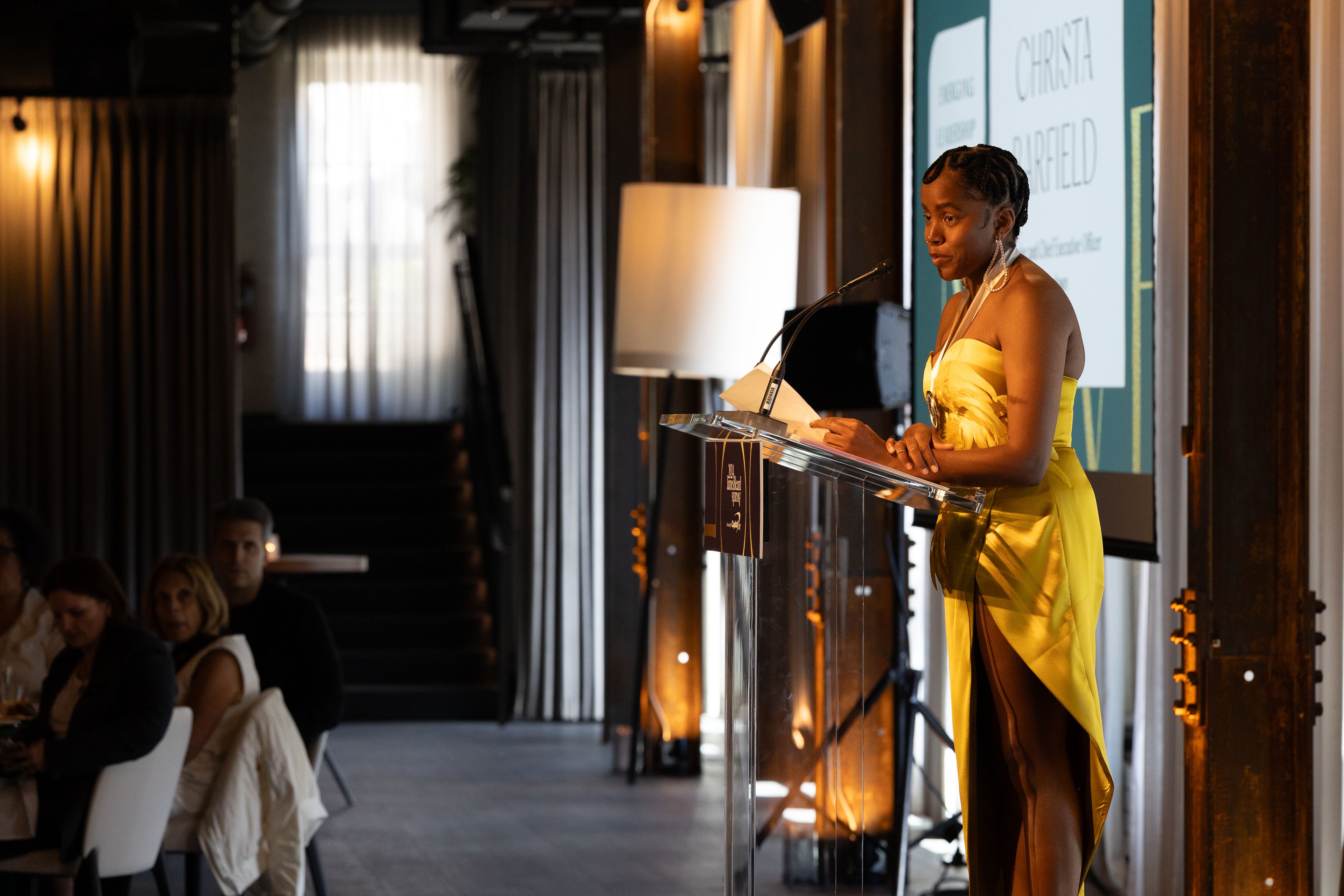 Woman in a yellow dress speaking at a podium