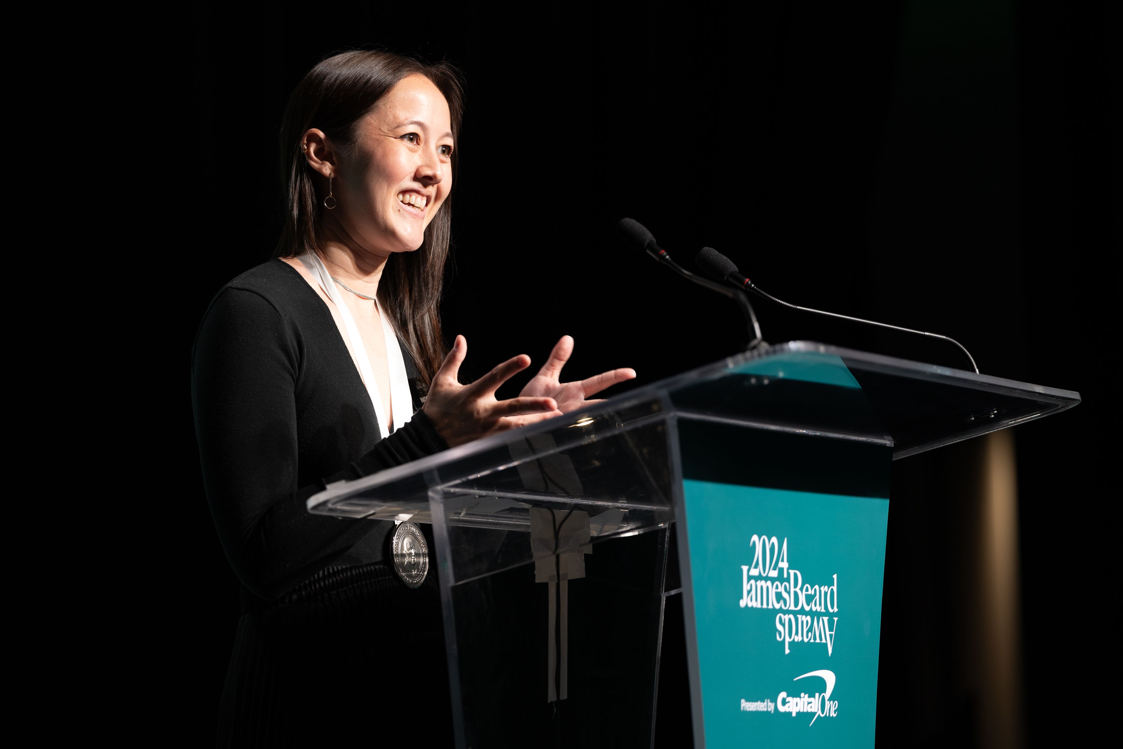 Shelby Lum with a James Beard Award medallion around her neck, standing at the podium