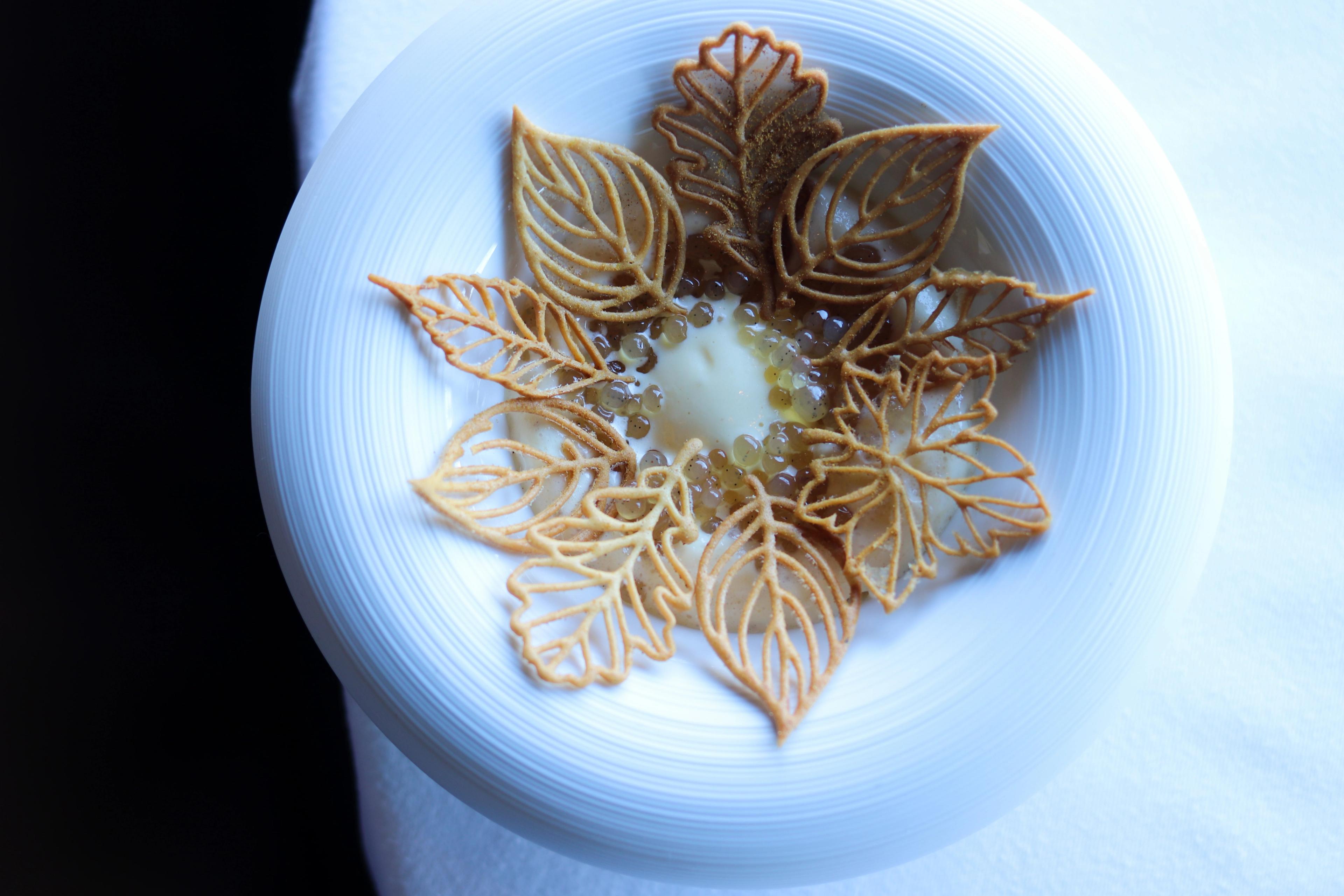 A bold white bowl with piped leaf shaped crackers, pearls, and foam