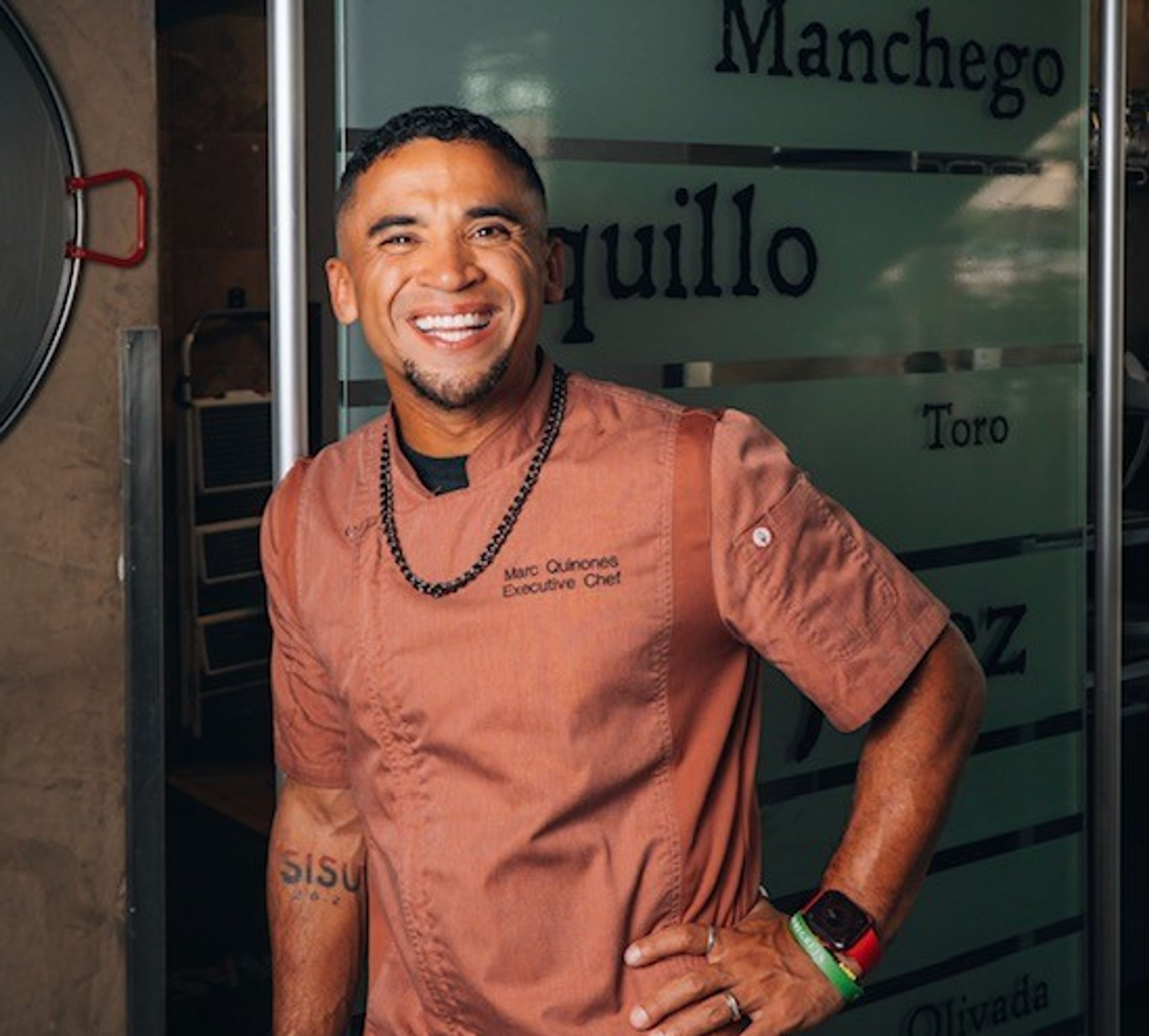 Marc Quinones smiling in an orange chef coat
