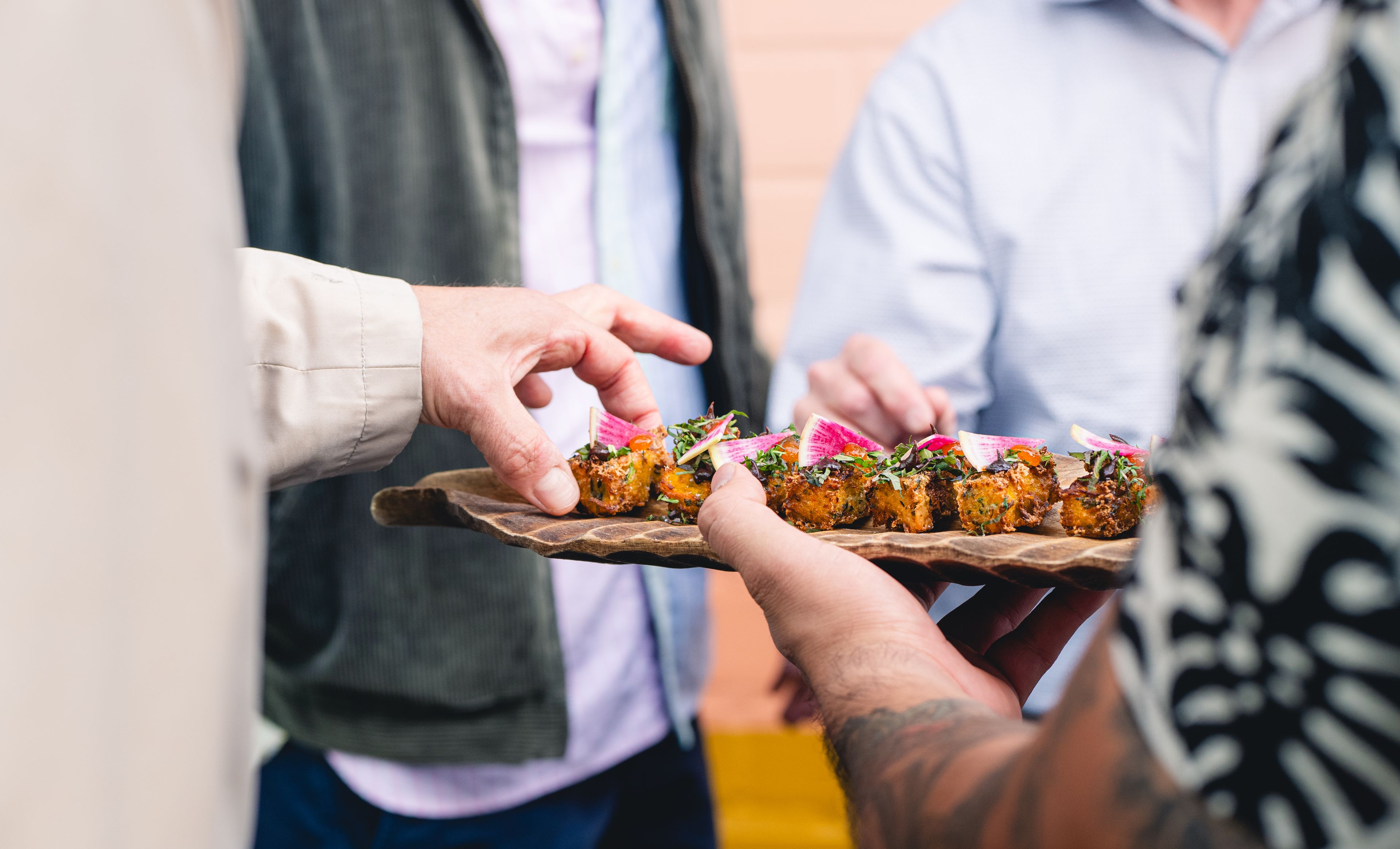 Hand reaching for appetizer on a wooden tray