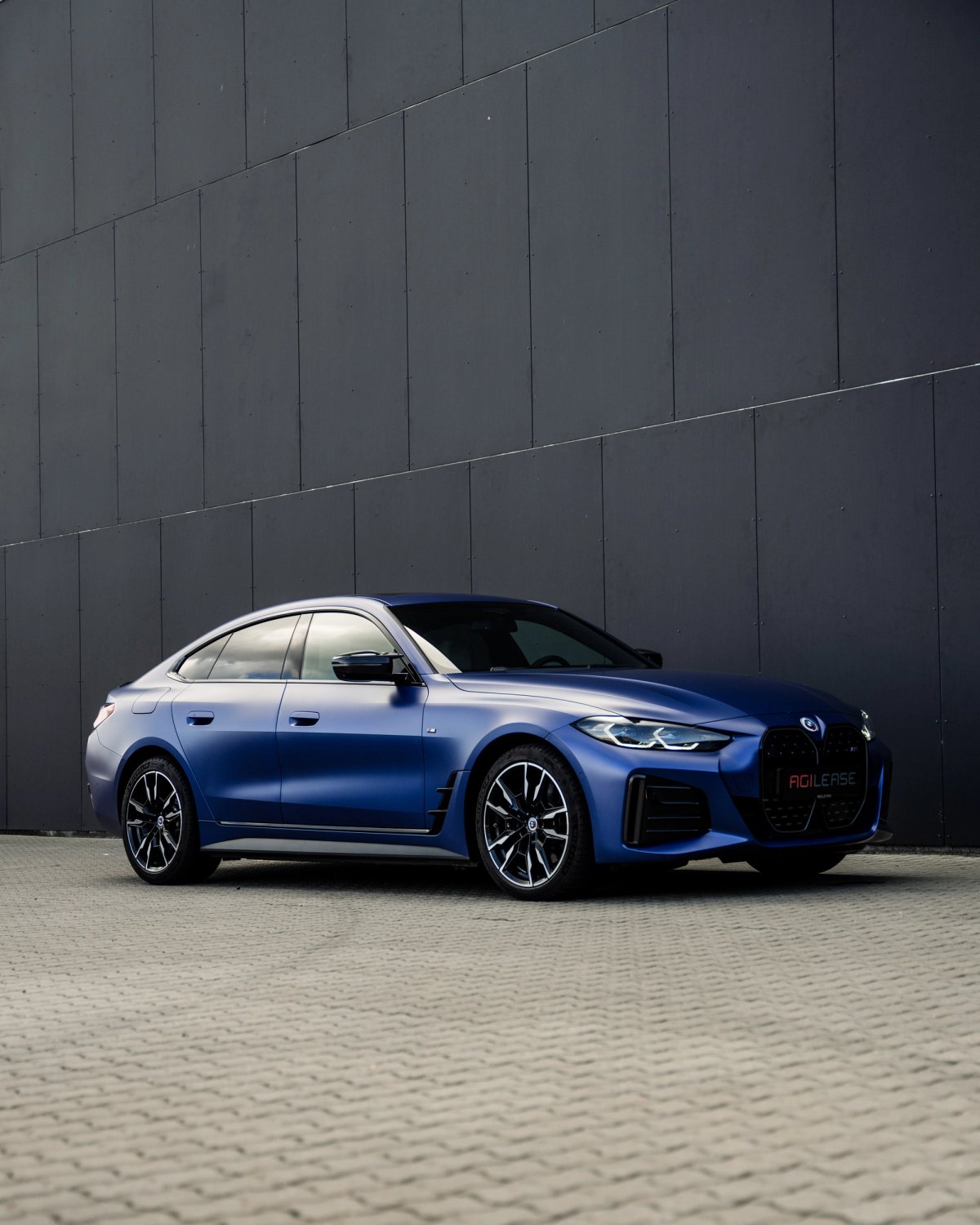 Blå BMW i4 M50 xDrive parkeret foran moderne bygning som firmabil med operationel leasing.