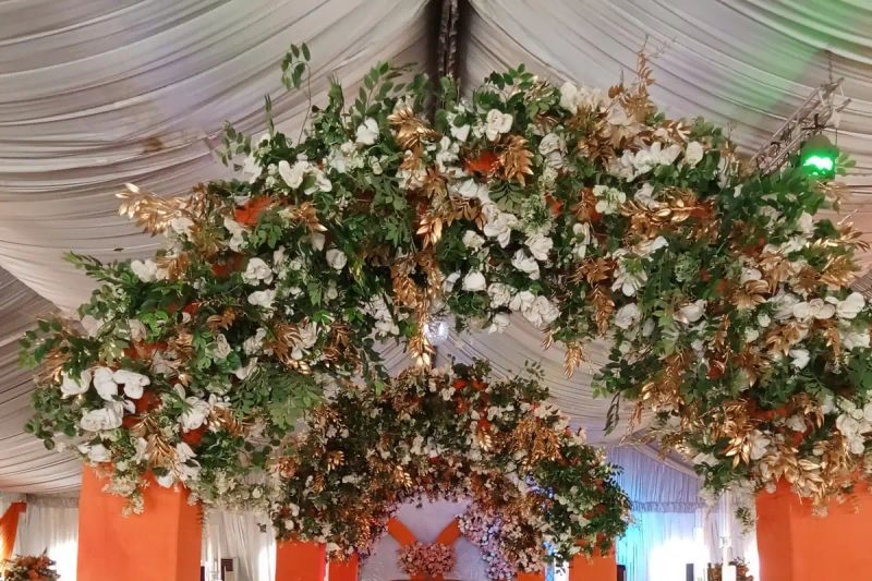 A flower covered arch over an orange draped aisle in a decorated hall