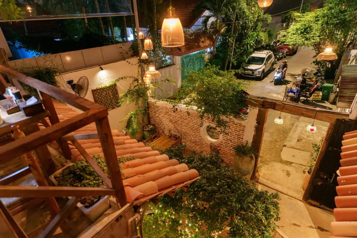 Không gian ngoài trời nhà hàng pizza Pazzi vào buổi tối với cầu thang gỗ, cây xanh trang trí, đèn treo ấm áp và view đường phố yên tĩnh