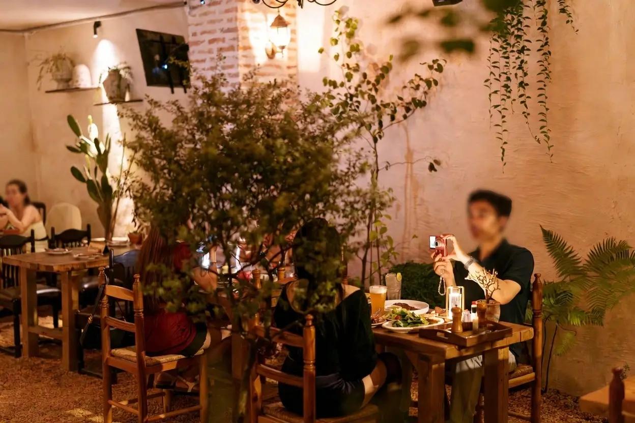 Không gian nhà hàng Pazzi với trang trí cây xanh, bàn gỗ, khách ăn tối và ánh sáng ấm áp