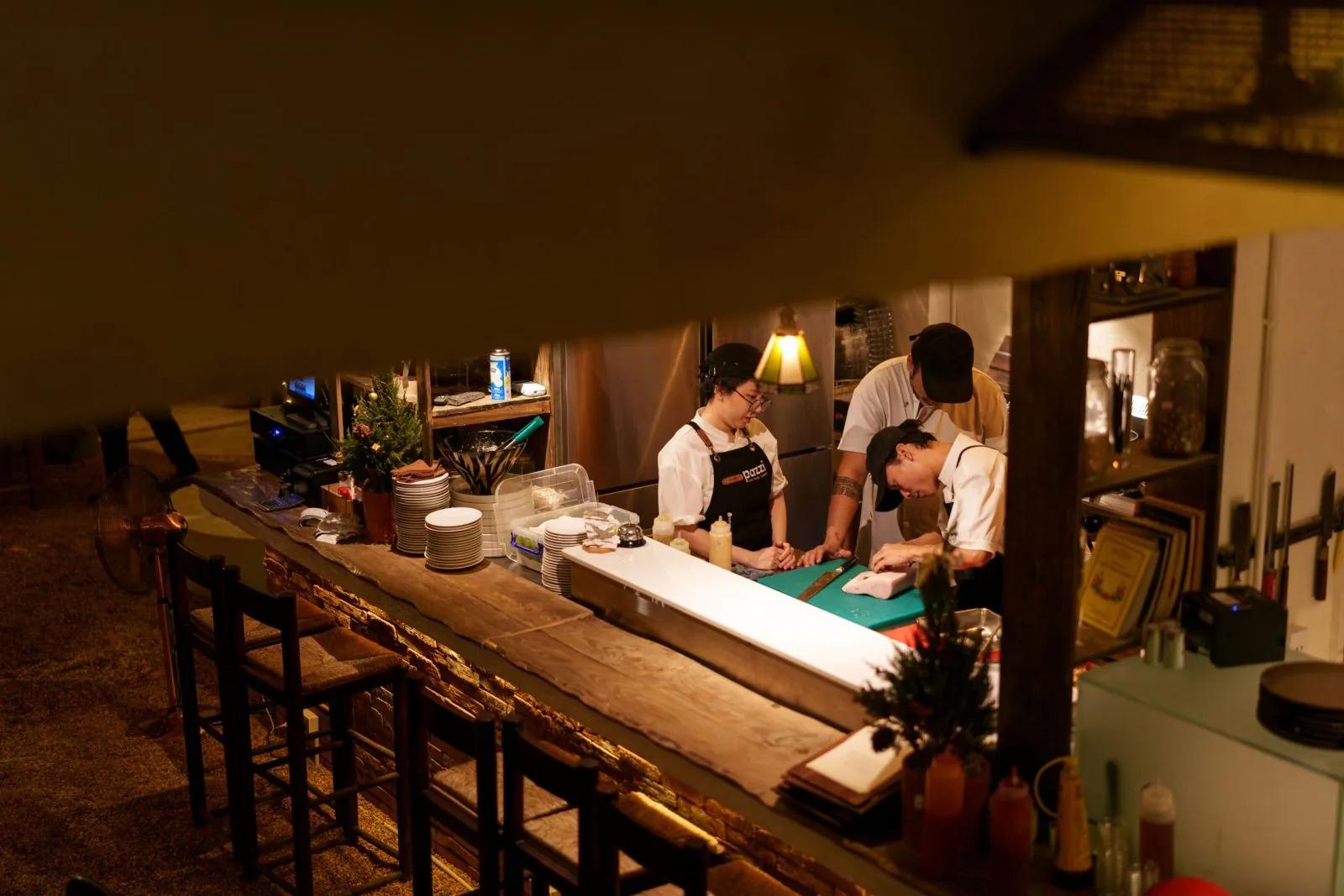 Nhân viên nhà hàng Pazzi đang chuẩn bị pizza tại quầy bếp mở, với đội ngũ chef chuyên nghiệp chuẩn bị nhân liệu pizza Ý truyền thống