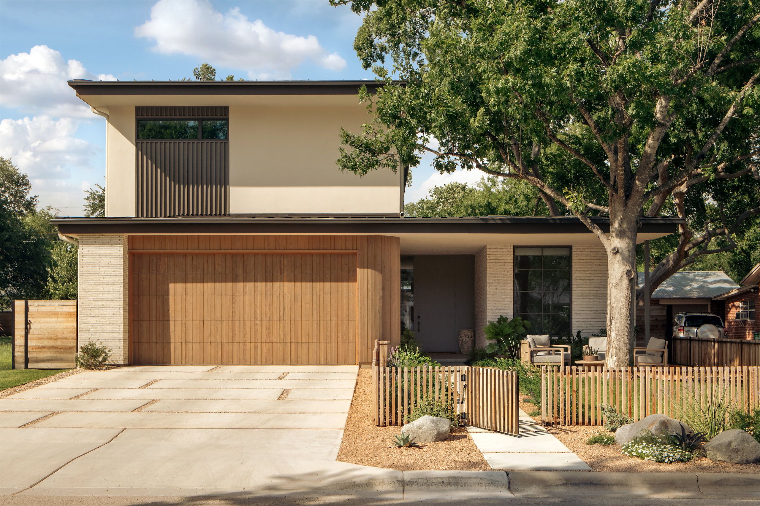 Two-story house with a wood garage door, a slatted fence, and a large tree