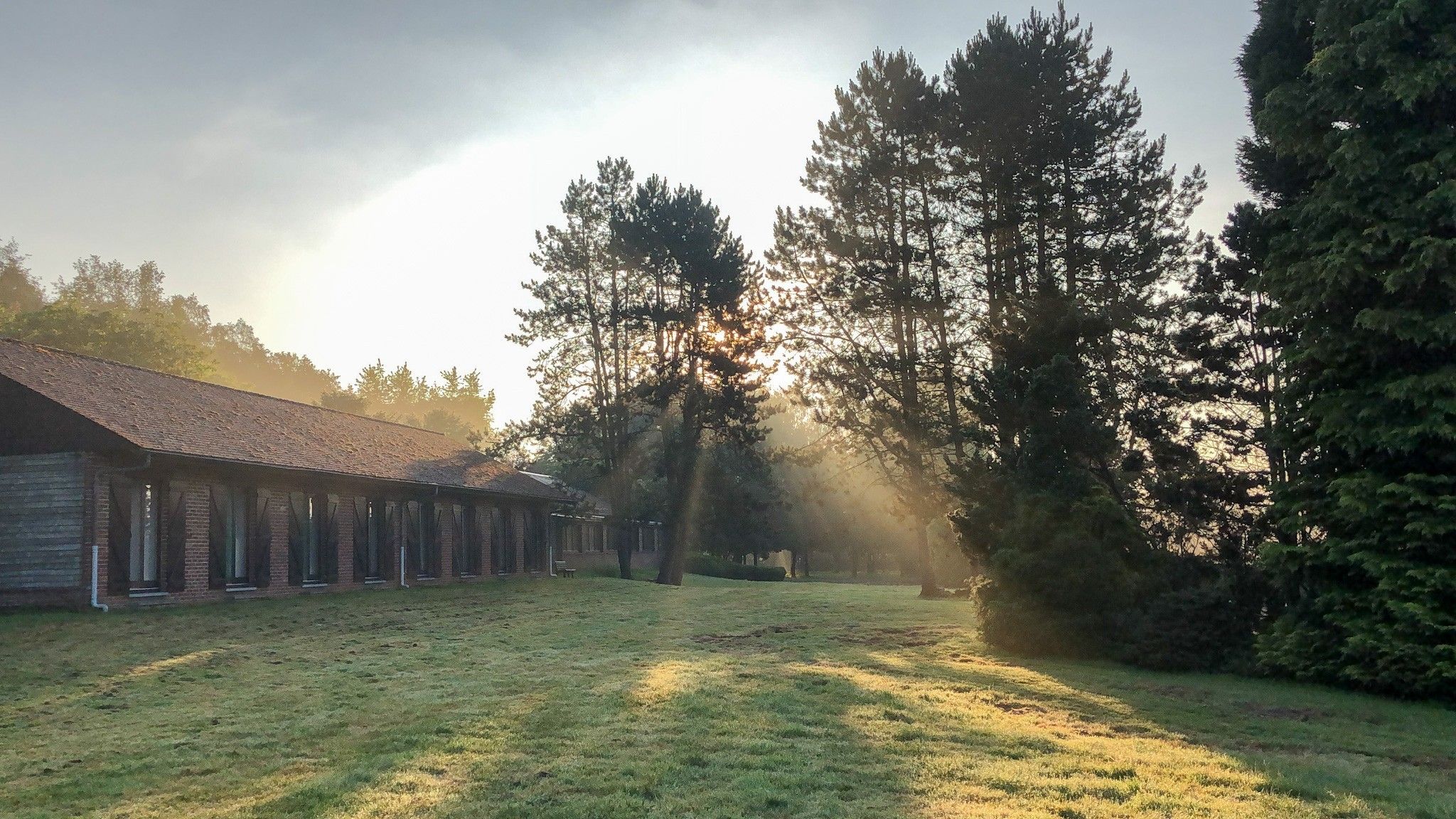 Zonsopgang boven het retraitecentrum in Brognon, met licht door de bomen over het gazon