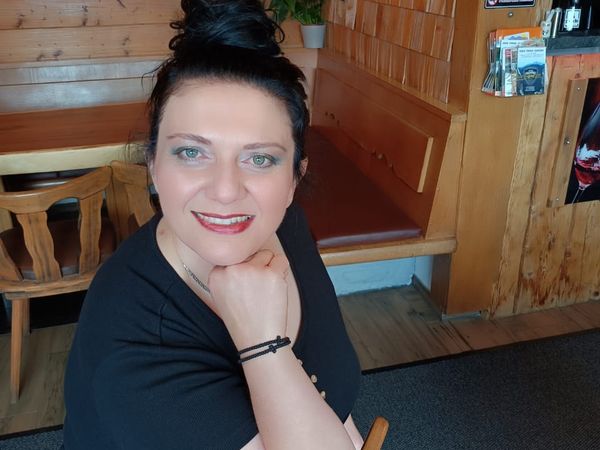 Marieta Sidiropoulou sitzt am Tisch im Gaichtpassstüberl, lächelt in die Kamera