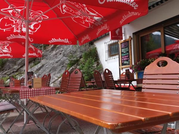 Terrasse des Gaichtpassstüberl mit roten Almdudler-Schirmen und Kreidetafel