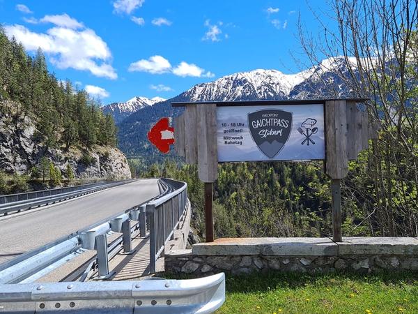 Hinweisschild am Brückengeländer: Gaichtpass Stüberl mit Öffnungszeiten, Berge im Hintergrund