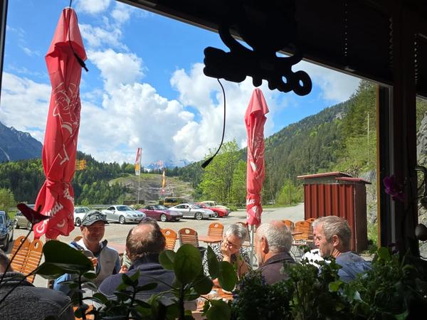 Blick aus dem Innenraum mit Motorrad-Deko auf die Terrasse mit Oldtimern