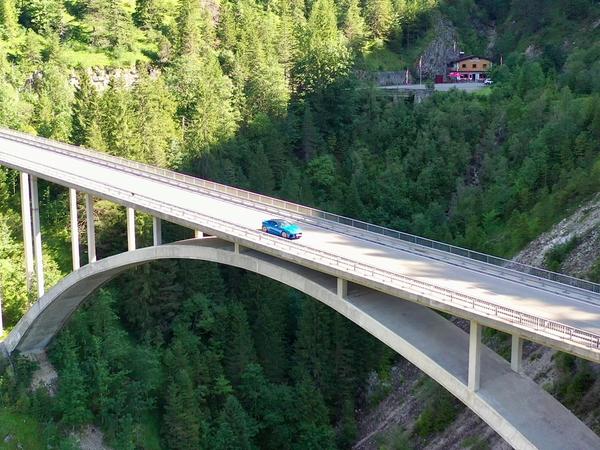 Drohnenaufnahme: Blauer Oldtimer auf der Gamstalbrücke, Stüberl klein im Hintergrund