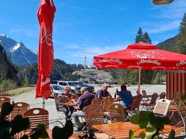 Blick durchs Fenster auf Terrasse und Bergpanorama, Gäste sitzen im Freien