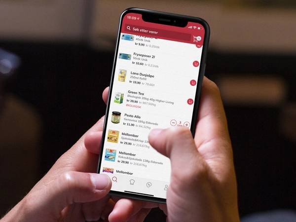 En person holder en smarttelefon som viser en app med ulike menyer og ikoner, sannsynligvis en mat- eller dagligvareapp.