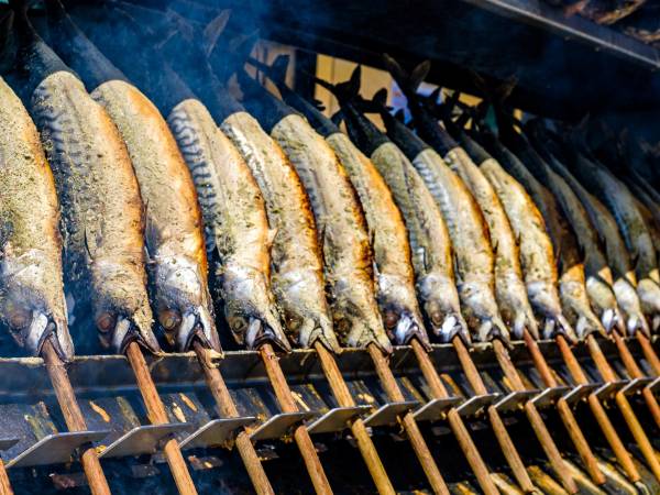 Fisk som grilles på en grill med røyksky i bakgrunnen.