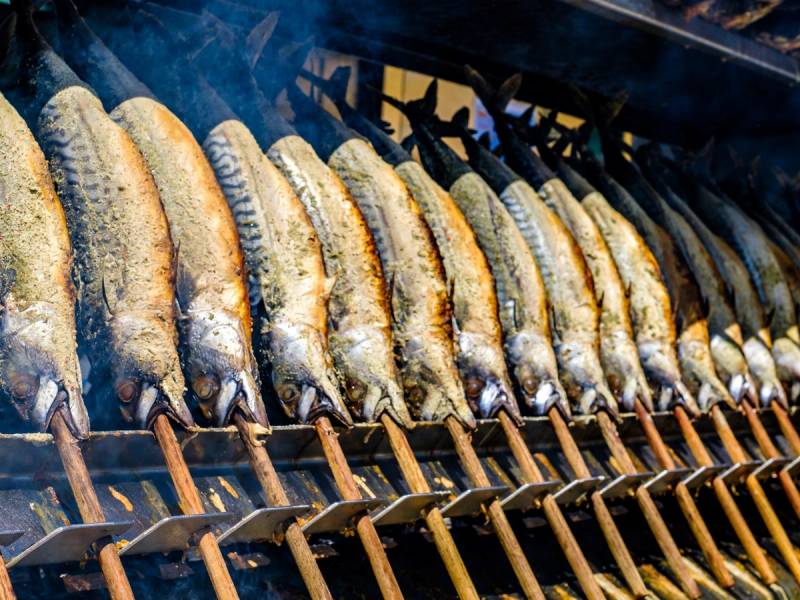 Fisk som grilles på en grill med røyksky i bakgrunnen.