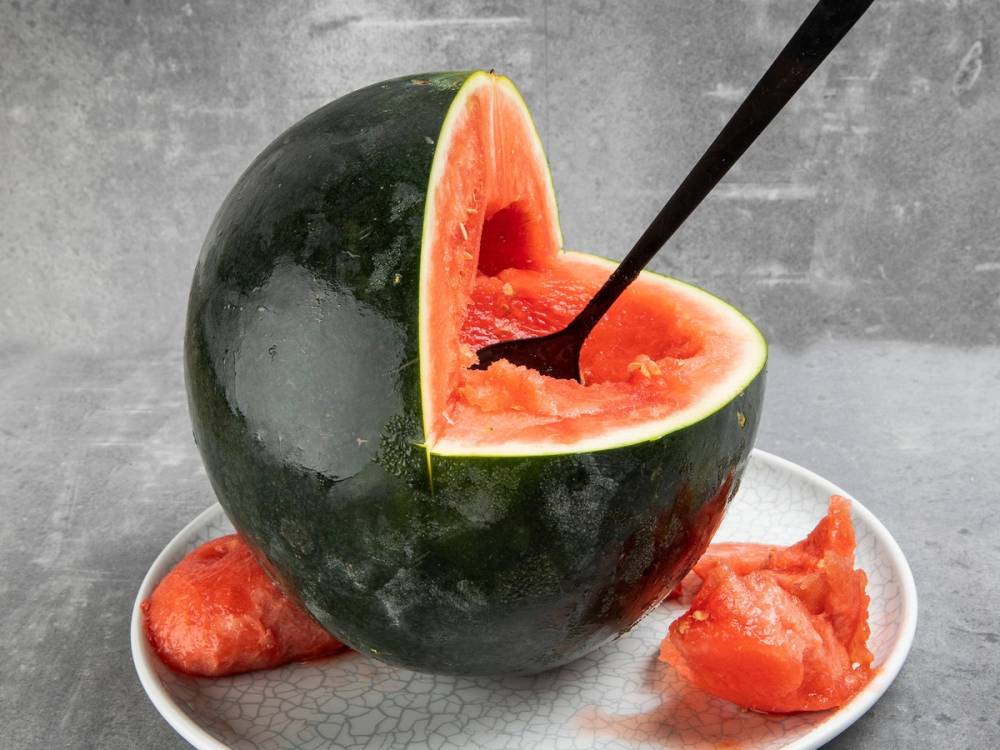 Vannmelon som er skåret ut og brukt som en skål, med en skje i, på en tallerken.