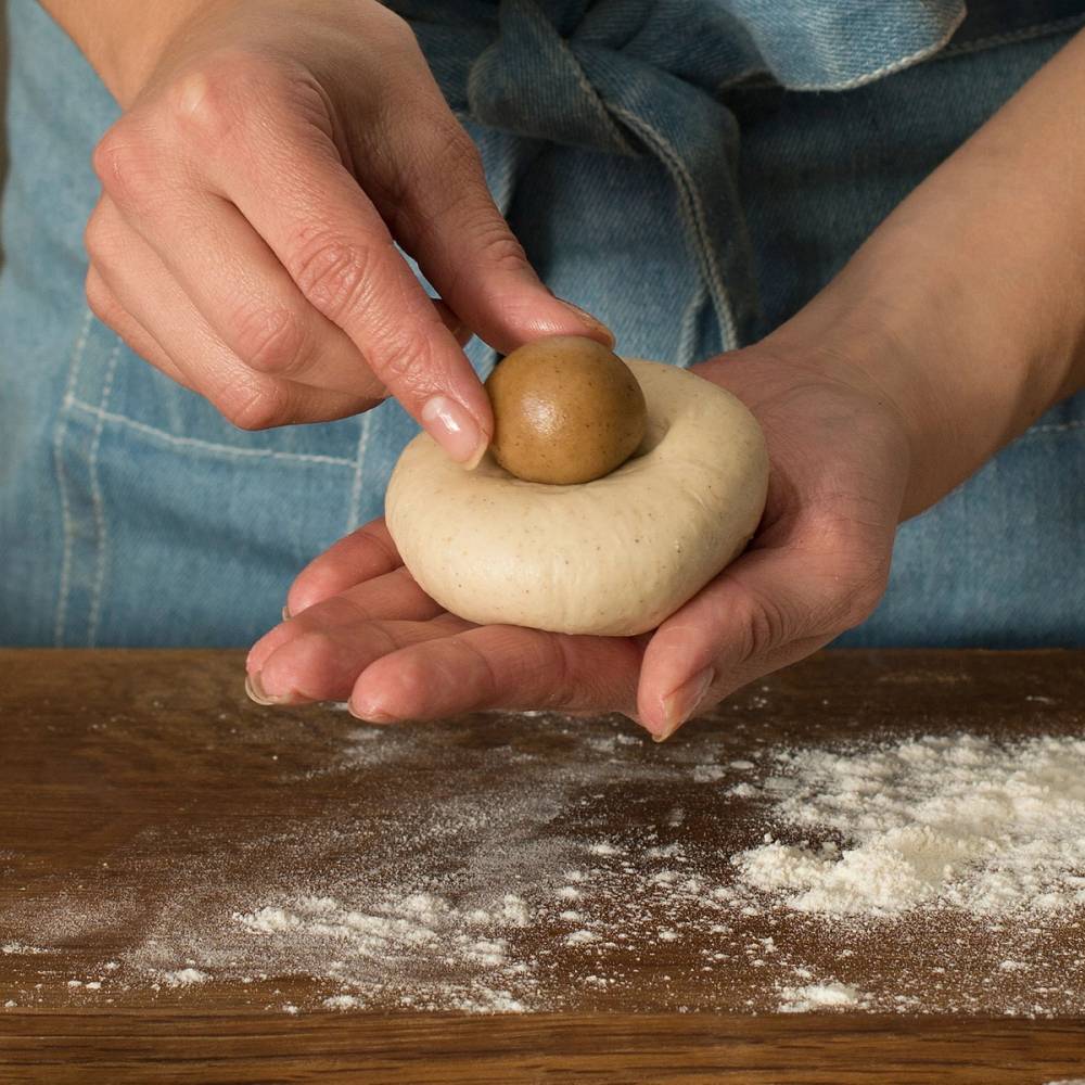 Person former pepperkakedeig til en ball på et bord med mel, med fokus på hendene og deigen.