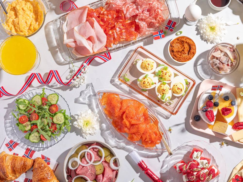 Frokostbord med norske flagg, eggerøre, røkelaks, grønnsalat, og diverse pålegg til 17. mai-feiring.