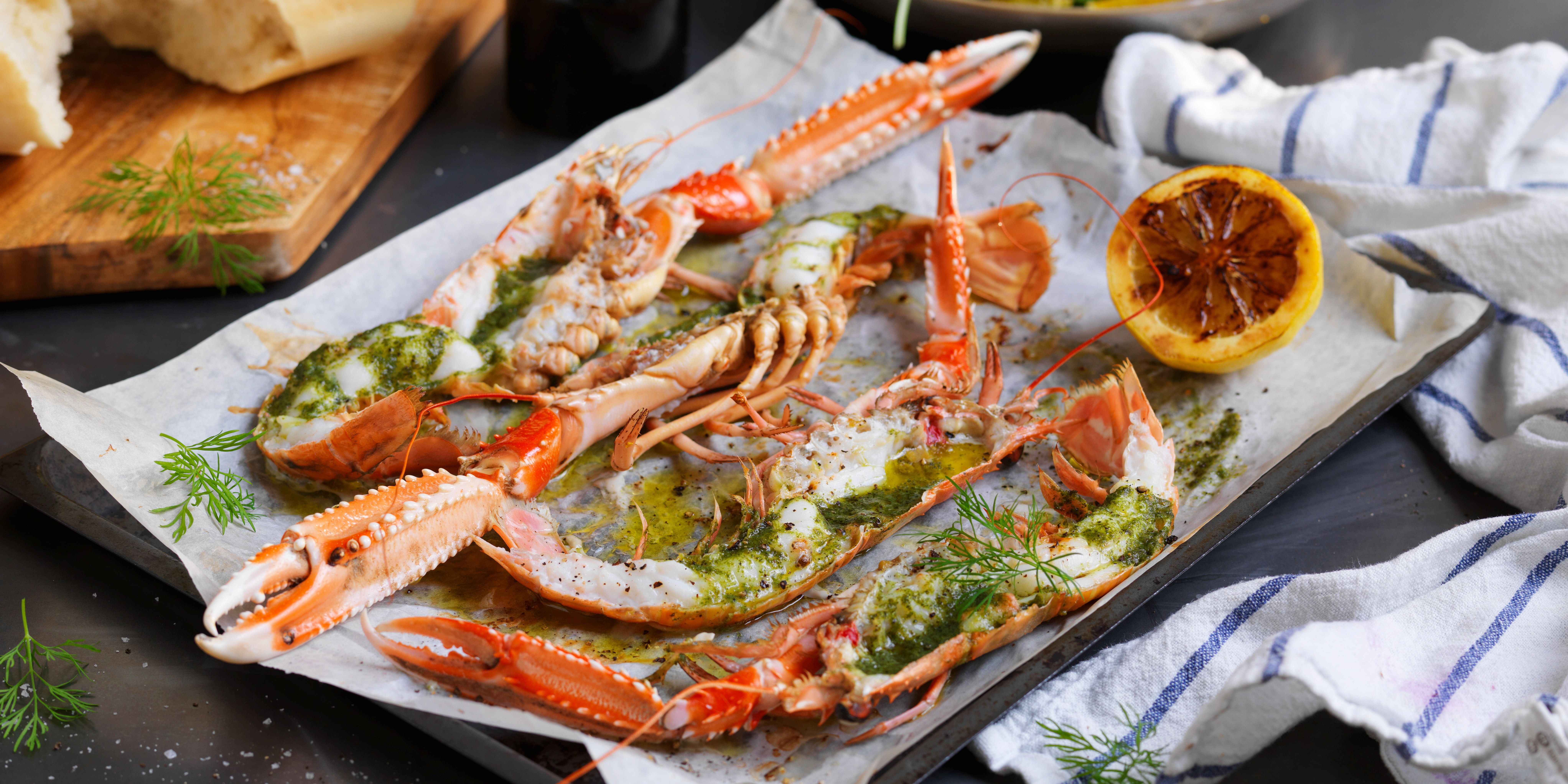 Gratinerte sjøkreps med ramsløksmør servert på et fat med sitronbåter og urter, klar til å nytes.