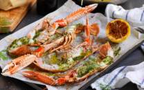 Gratinerte sjøkreps med ramsløksmør servert på et fat med sitronbåter og urter, klar til å nytes.