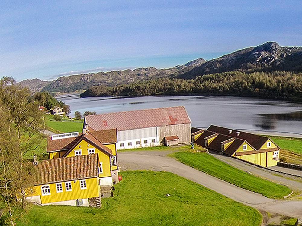 Fargerike hus ved en innsjø med fjell i bakgrunnen, omgitt av grønt landskap.