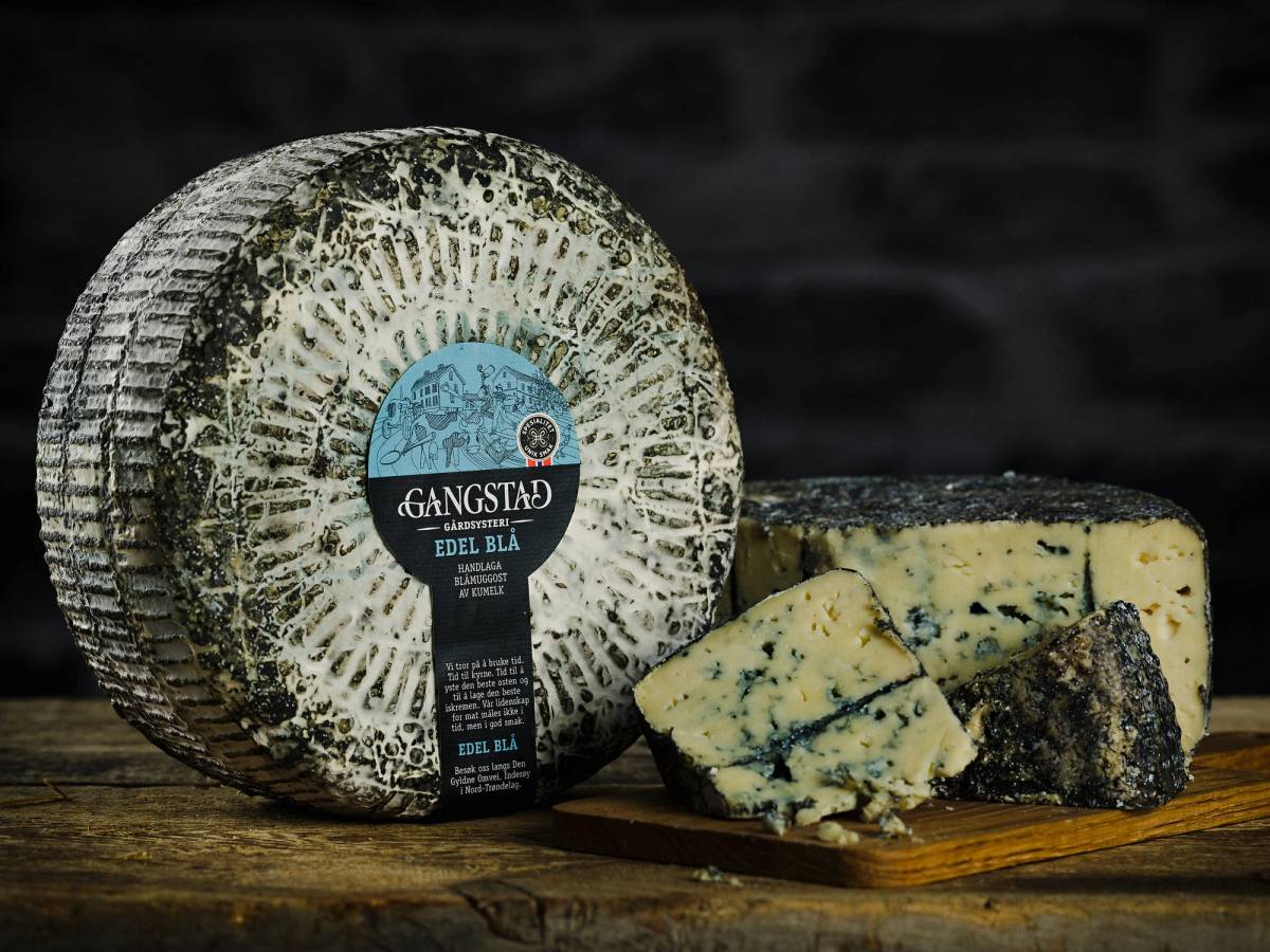 Edel blå ost med blåmugg og en skive som er kuttet opp, plassert på et trebrett mot en mørk bakgrunn.