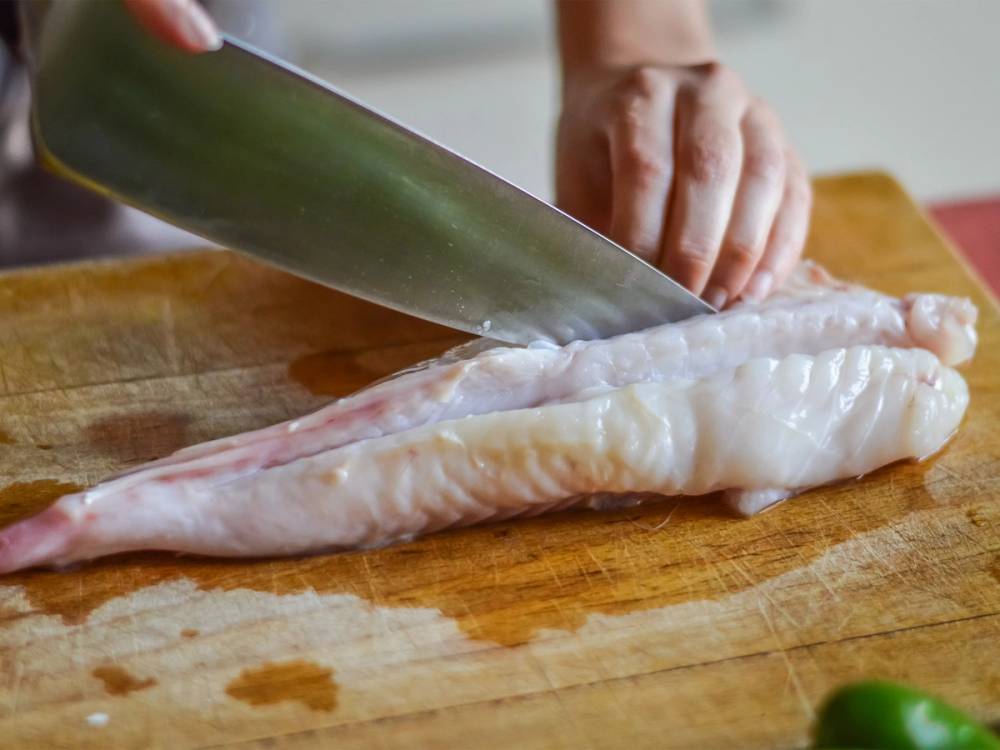 En person skjærer i en breiflabb på et skjærebrett med en stor kniv.