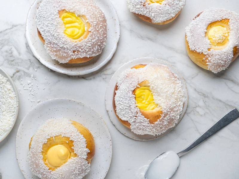 Boller med skolebrød-fyll og kokos på toppen, ser ut til å være på en hvit tallerken med en skje ved siden av.