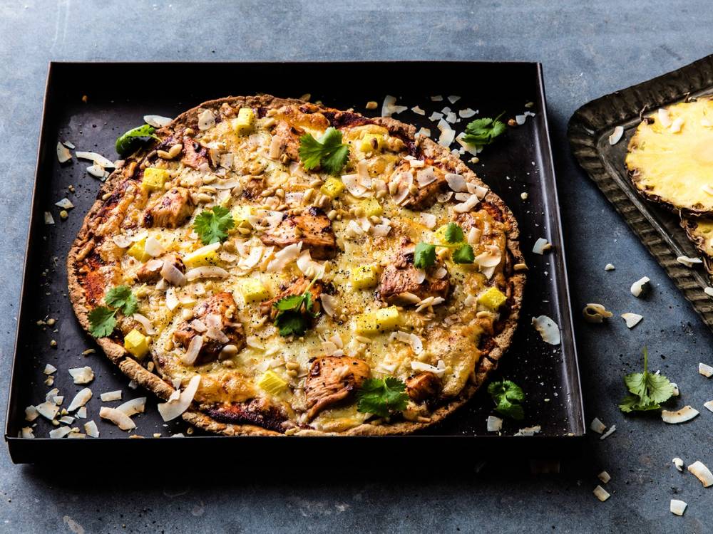 Kyllingpizza med ost, kyllingbiter og grønne urter på en svart pizzabunn, ser ut til å være fersk og varm.