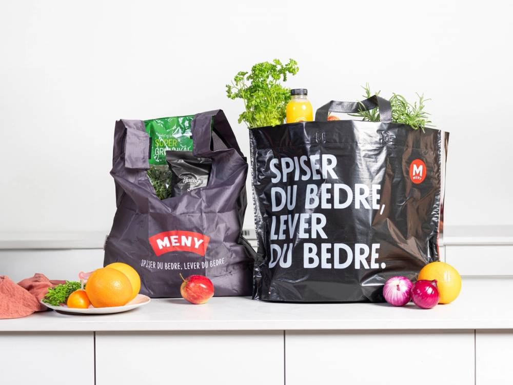 Gjenbruksposer i miljøvennlige handleposer med frukt og grønnsaker rundt på en hvit overflate.