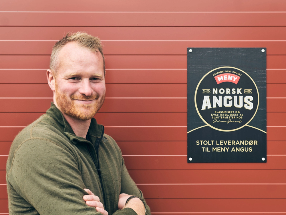 En person står foran en rød vegg med en plakat som reklamerer for Norsk Angus, med armene krysset.