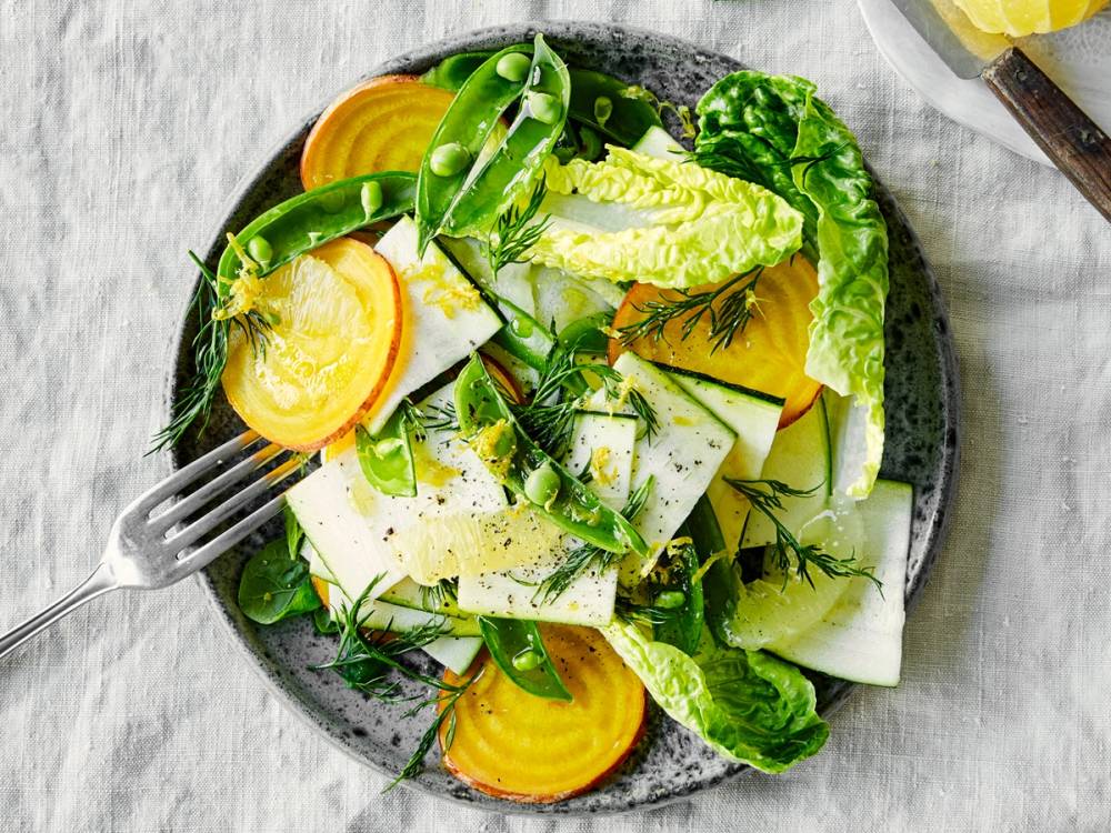 En salat med sitrusfrukter og rødbeter, servert på en svart tallerken med en gaffel ved siden av.