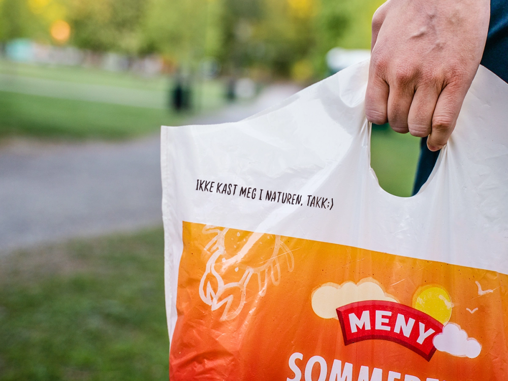 En person holder en plastpose med sommermerke i en park med grønt gress og trær i bakgrunnen.