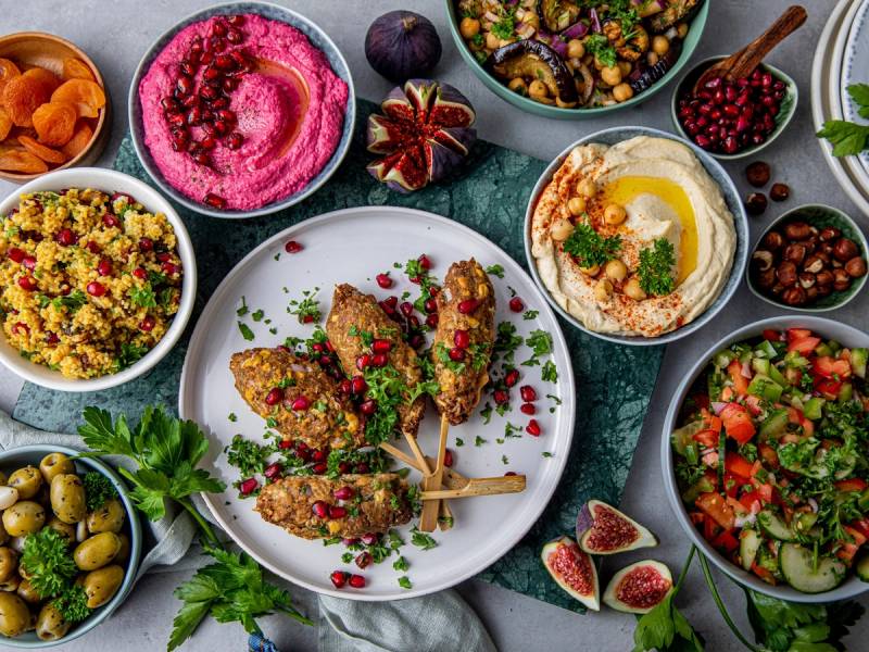Et utvalg av ulike salater og småretter på bordet, inkludert hummus, quinoa-salat, og grønnsaksretter, med noen fiken og bær som pynt.