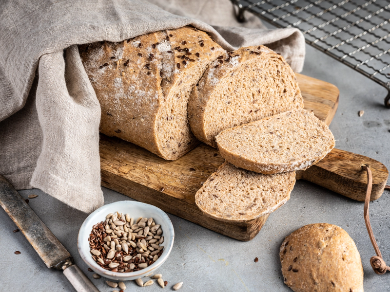 Tørt gammelt brød på et skjærebrett med en liten skål med nøtter ved siden av.