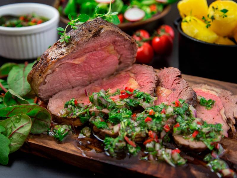 Perfekt stekt biff med grønn saus og tilbehør som poteter og tomater på et serveringsfat.