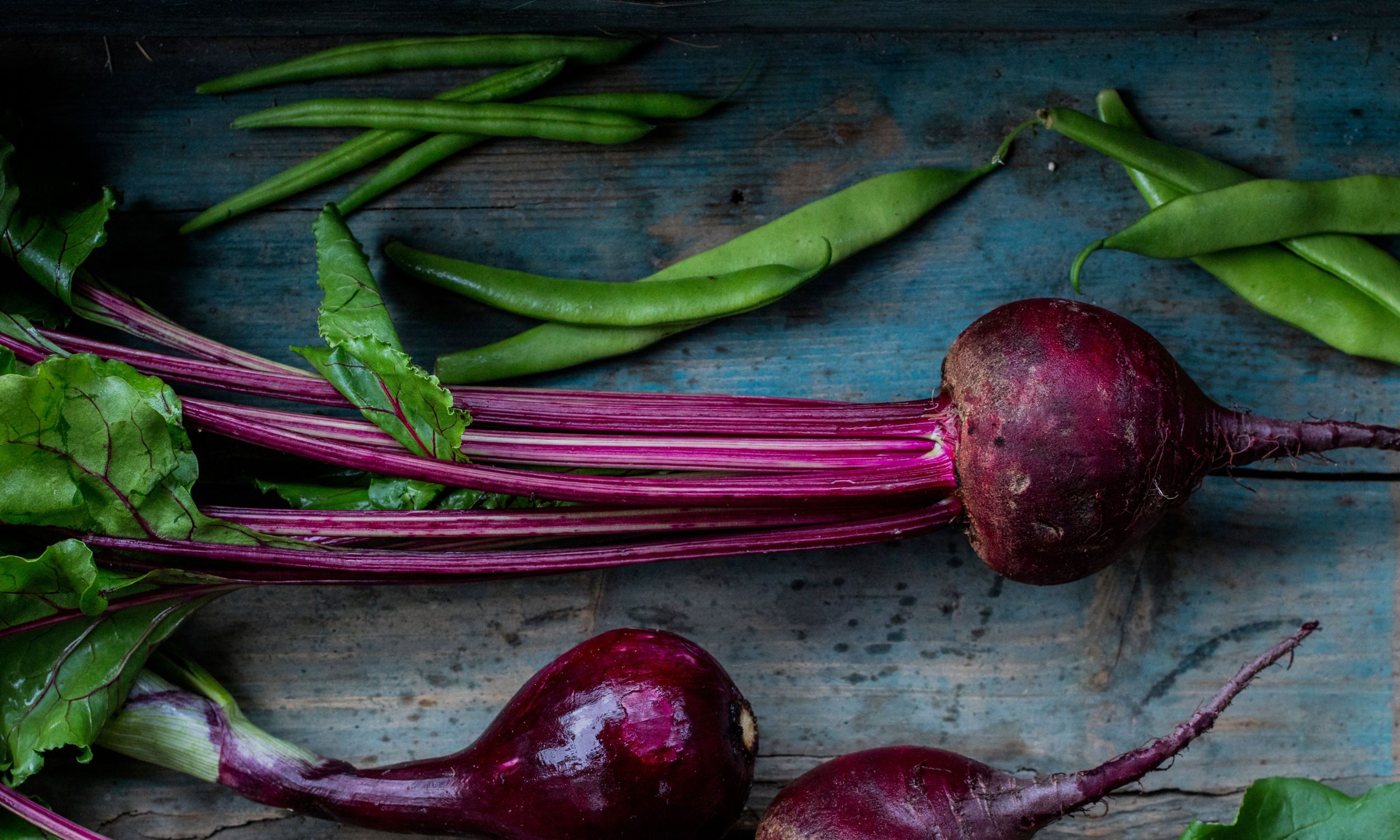 Rødbeter med grønne stilker ligger på en treplate, klare til å bli brukt i matlaging.