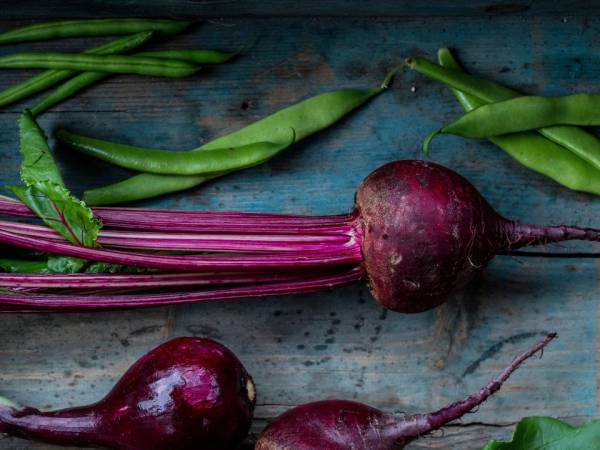Rødbeter med grønne stilker ligger på en treplate, klare til å bli brukt i matlaging.