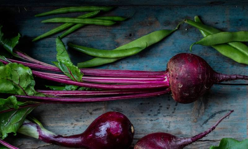 Rødbeter med grønne stilker ligger på en treplate, klare til å bli brukt i matlaging.