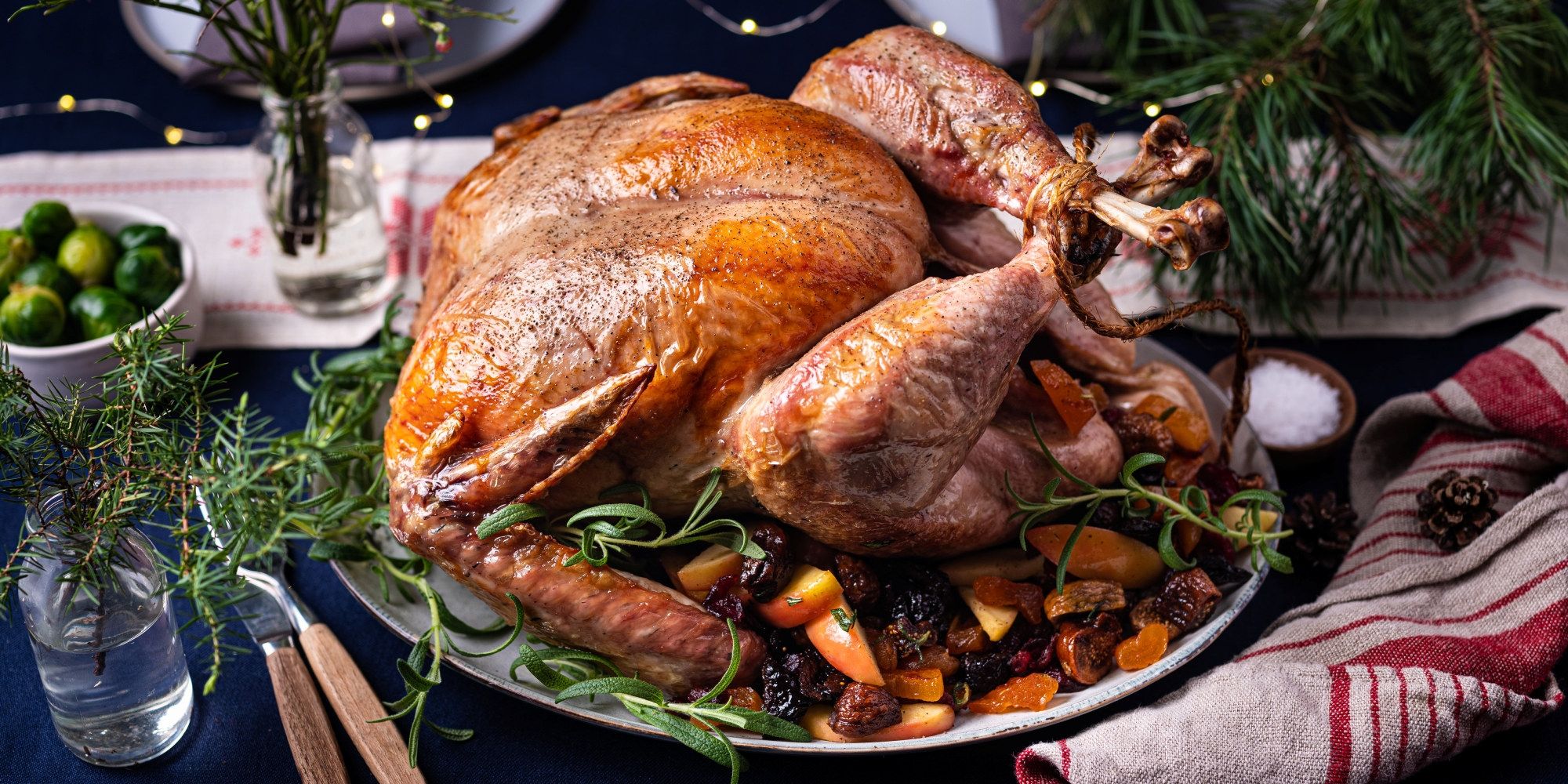 Stekt kalkun med grønnsaker og urter på et serveringsfat, omgitt av juledekorasjoner.