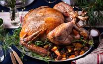 Stekt kalkun med grønnsaker og urter på et serveringsfat, omgitt av juledekorasjoner.
