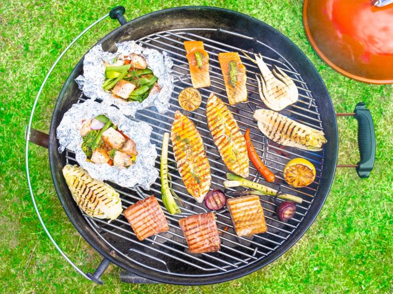 Grill med ulike fiskestykker, skalldyr og grønnsaker på en gressplen, klar for servering.